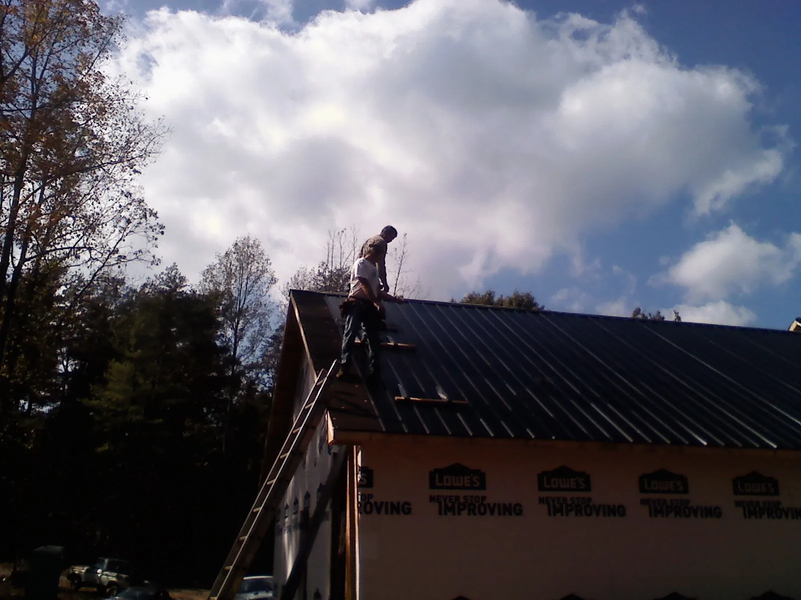 Roofer fastening dark metal panels high against a cloudy sky, from a Roof Inspection job in Humptulips