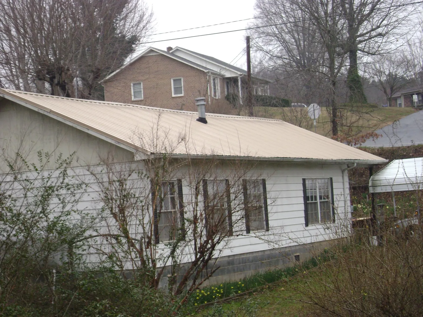Tan metal roof on a white sided house set into a hillside — Commercial Roofing by Roofing Brothers in Humptulips